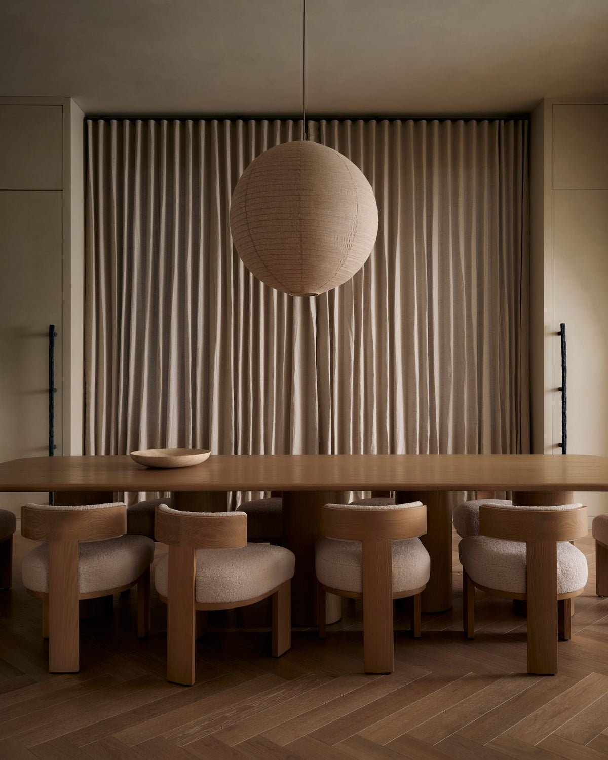 Linen globe pendant glowing above a long dining table with curved upholstered chairs