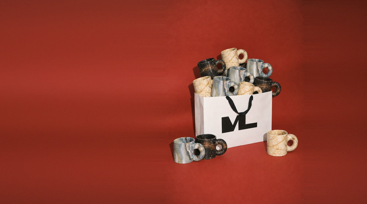 Marble mugs piled in a white Montana Labelle shopping bag on a red backdrop