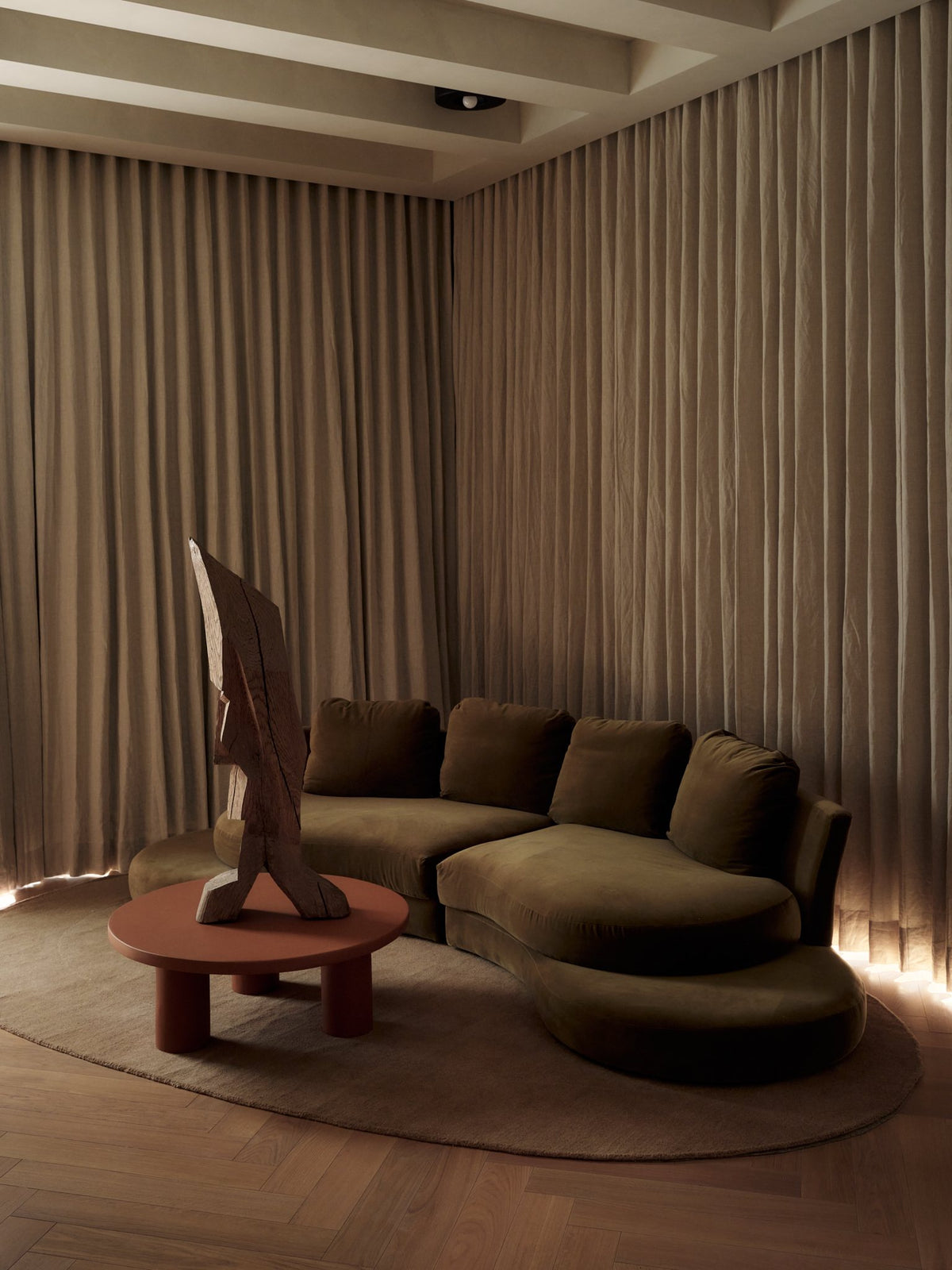 Lounge with a curved sofa, low wood coffee table, sculptural chair and softly draped walls in warm light