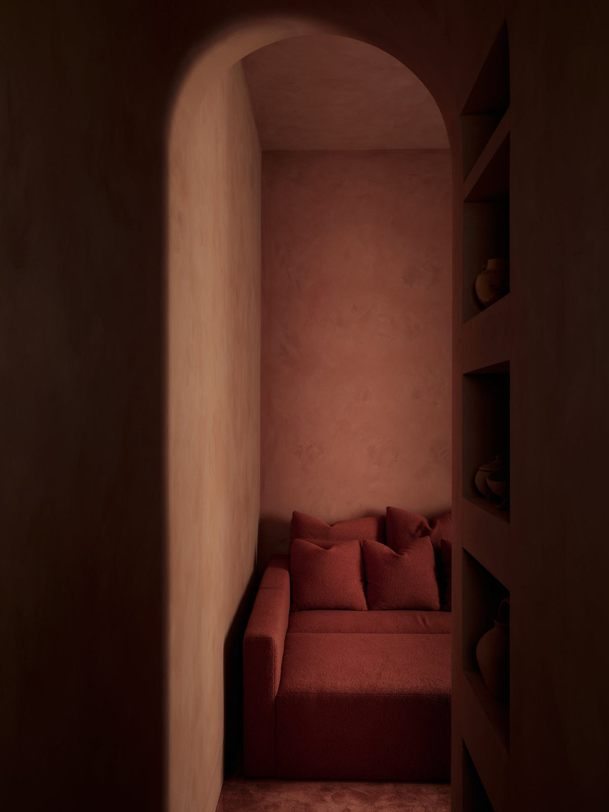Arched alcove with a red upholstered bench and cushions framed by deep red plaster walls