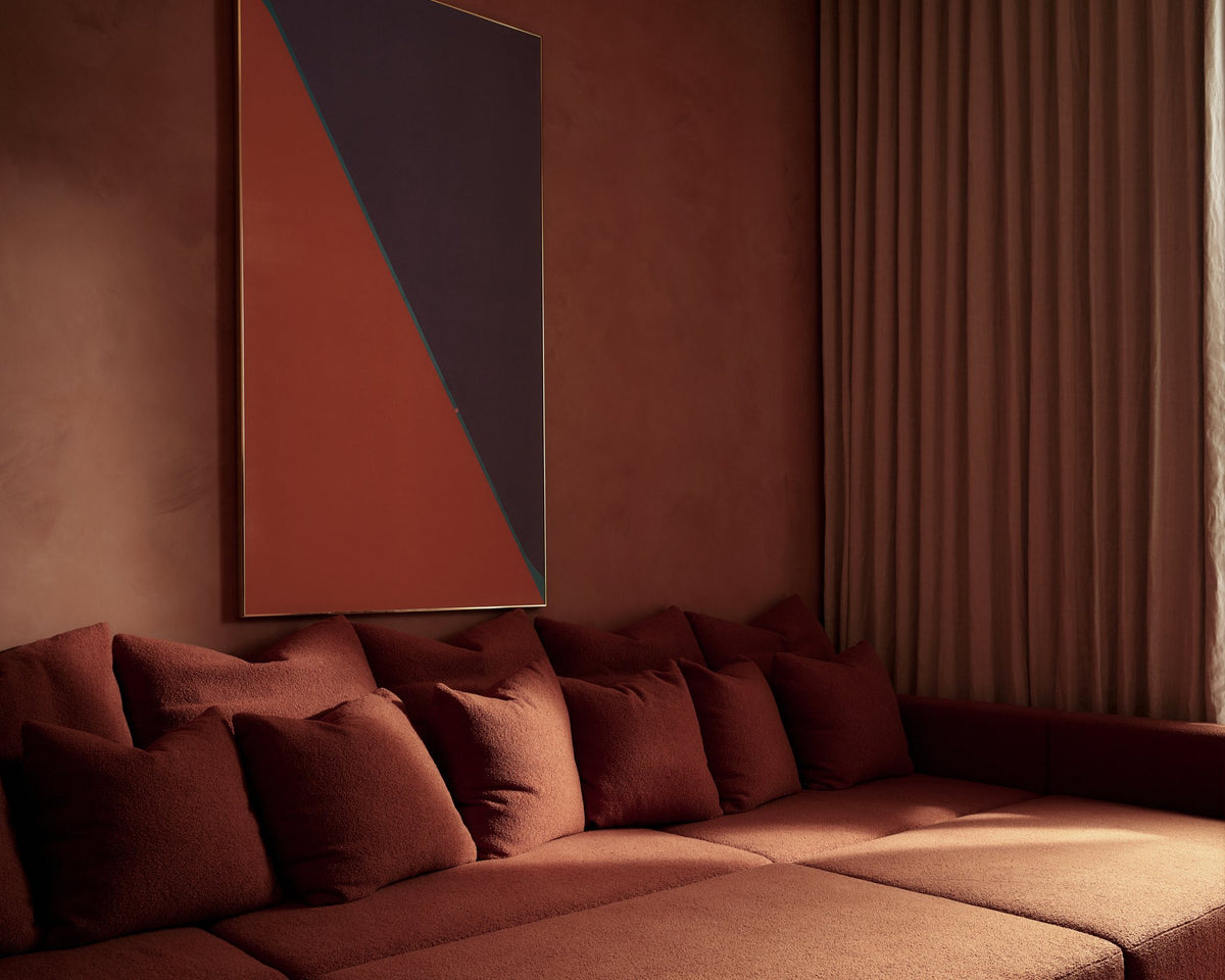 Terracotta living room with a deep low sofa, plush red cushions and full-length drapery