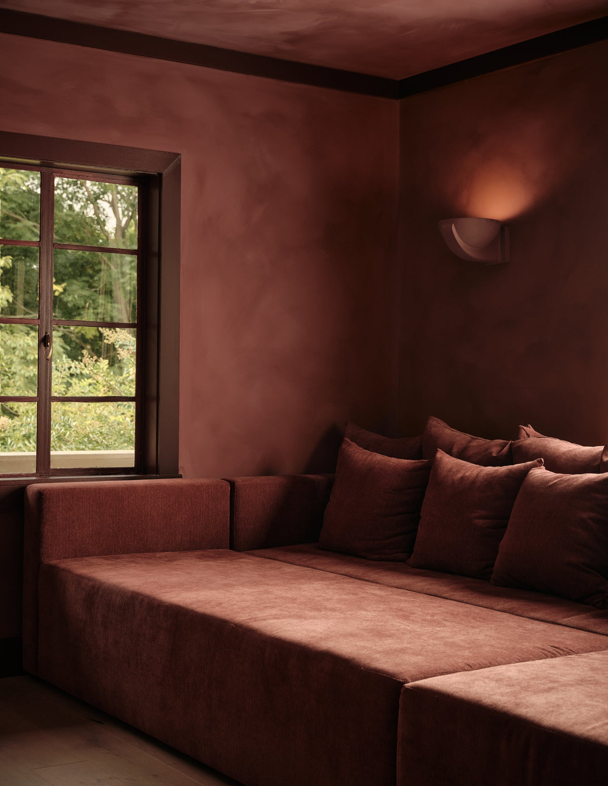 Brendan Plaster Sconce glowing on a red plaster wall above a built-in window-seat sofa