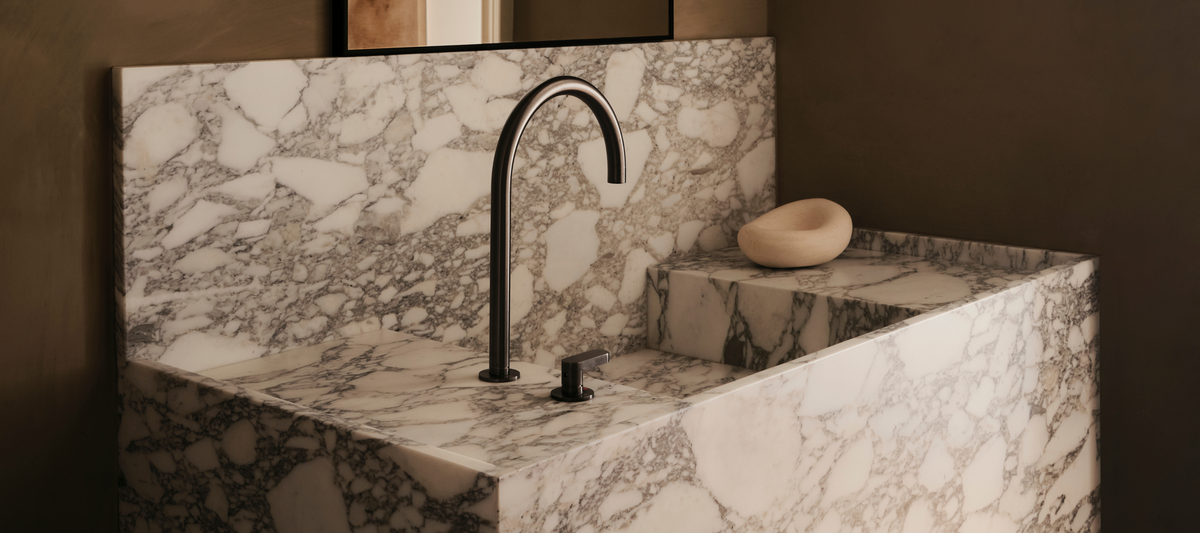 A marble vanity with a curved spout and a carved stone dish