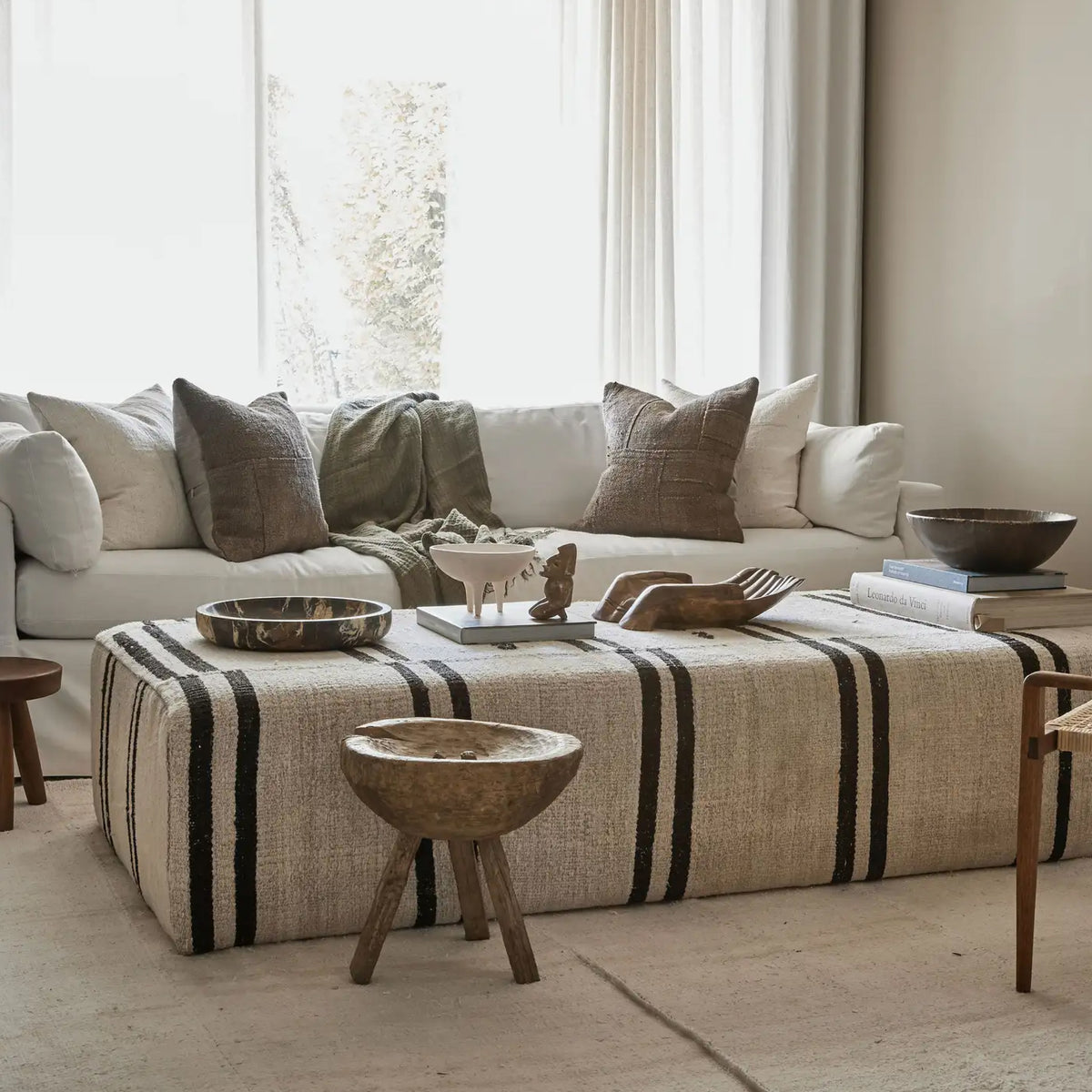 Living room styled with a striped sofa, round wood side table and sculptural vases