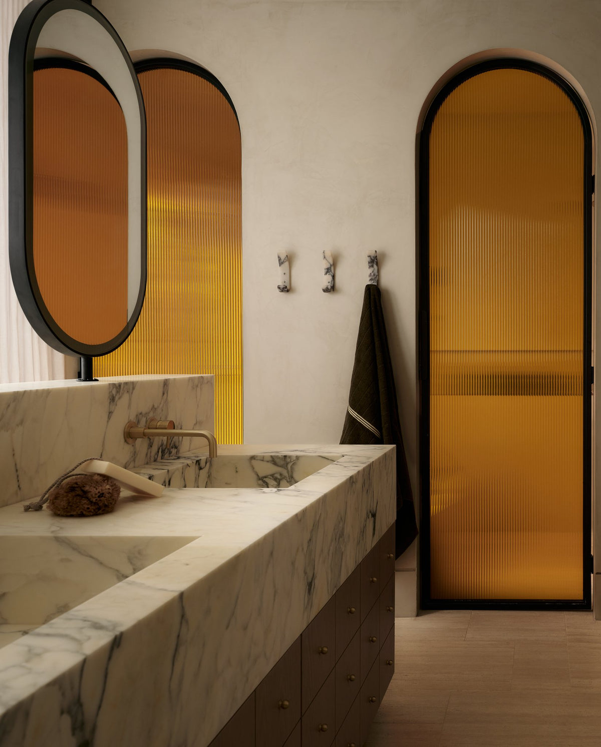 Marble vanity and Longbeach marble hooks beside an amber arched door