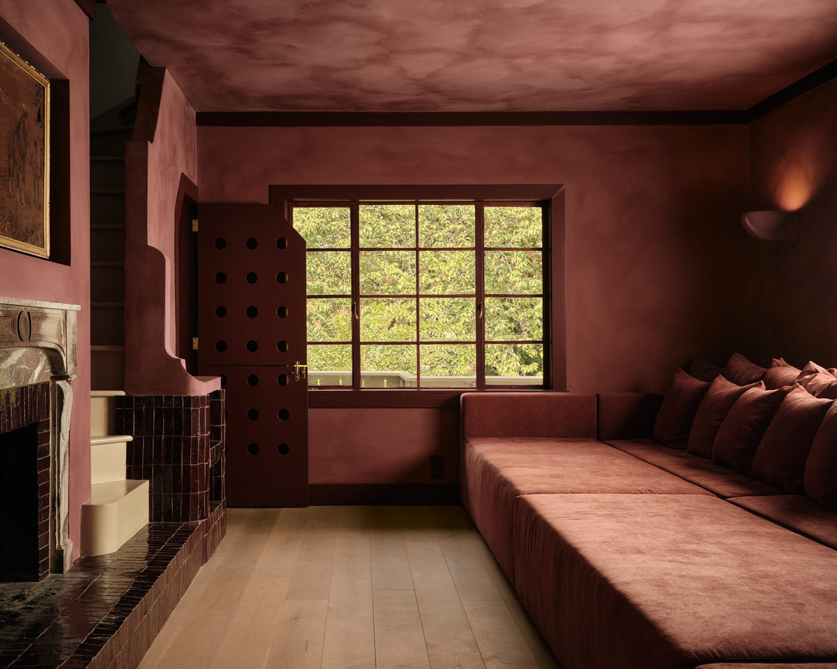 A terracotta sitting room with a low sofa and deep window seat
