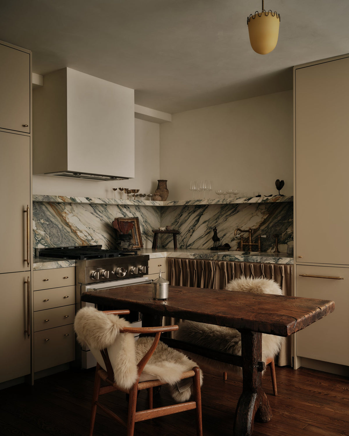 Kitchen with a marble backsplash, plaster hood and oak dining table with shearling-draped chairs