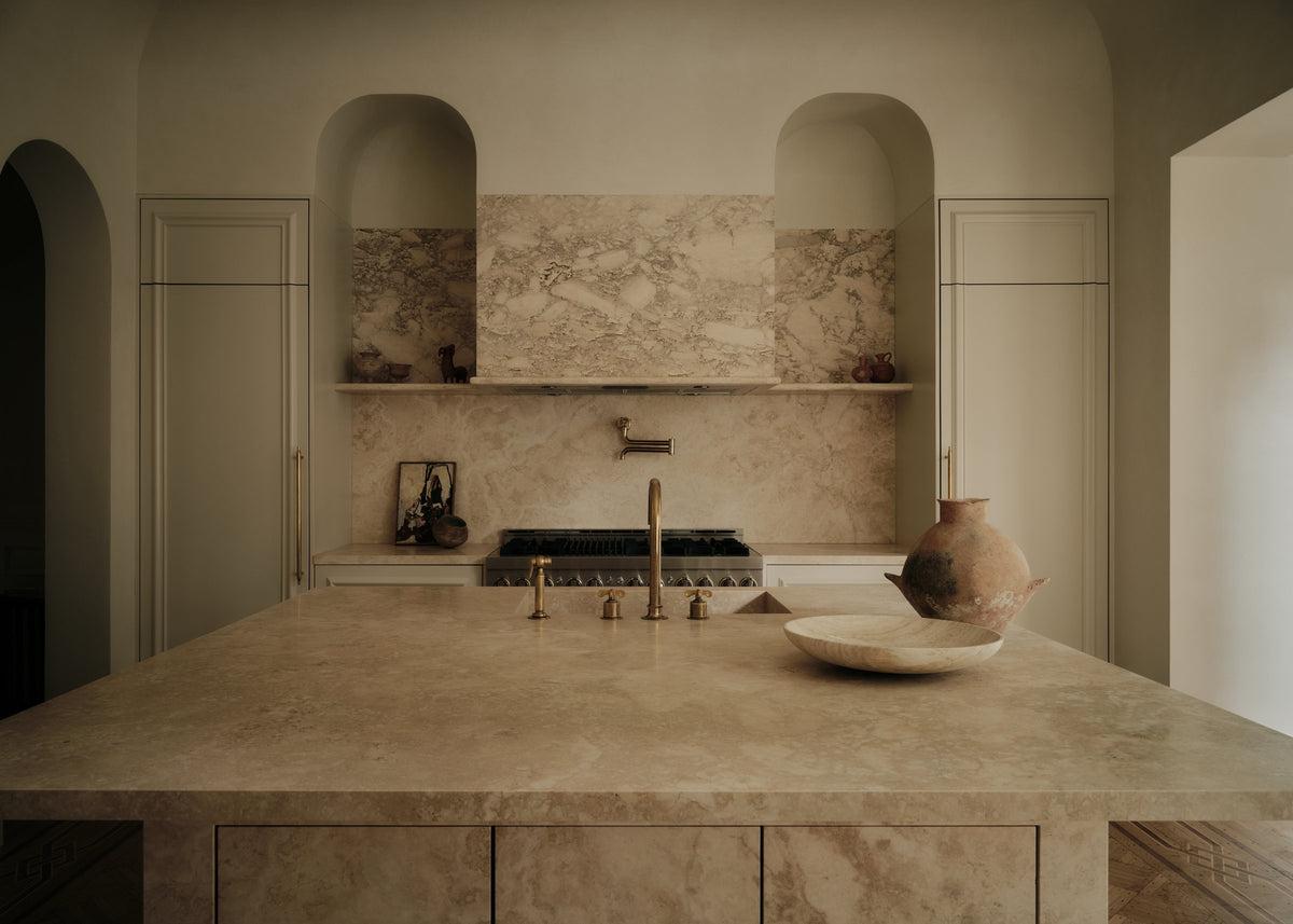 Kitchen with a stone island, arched plaster niches and a marble backsplash