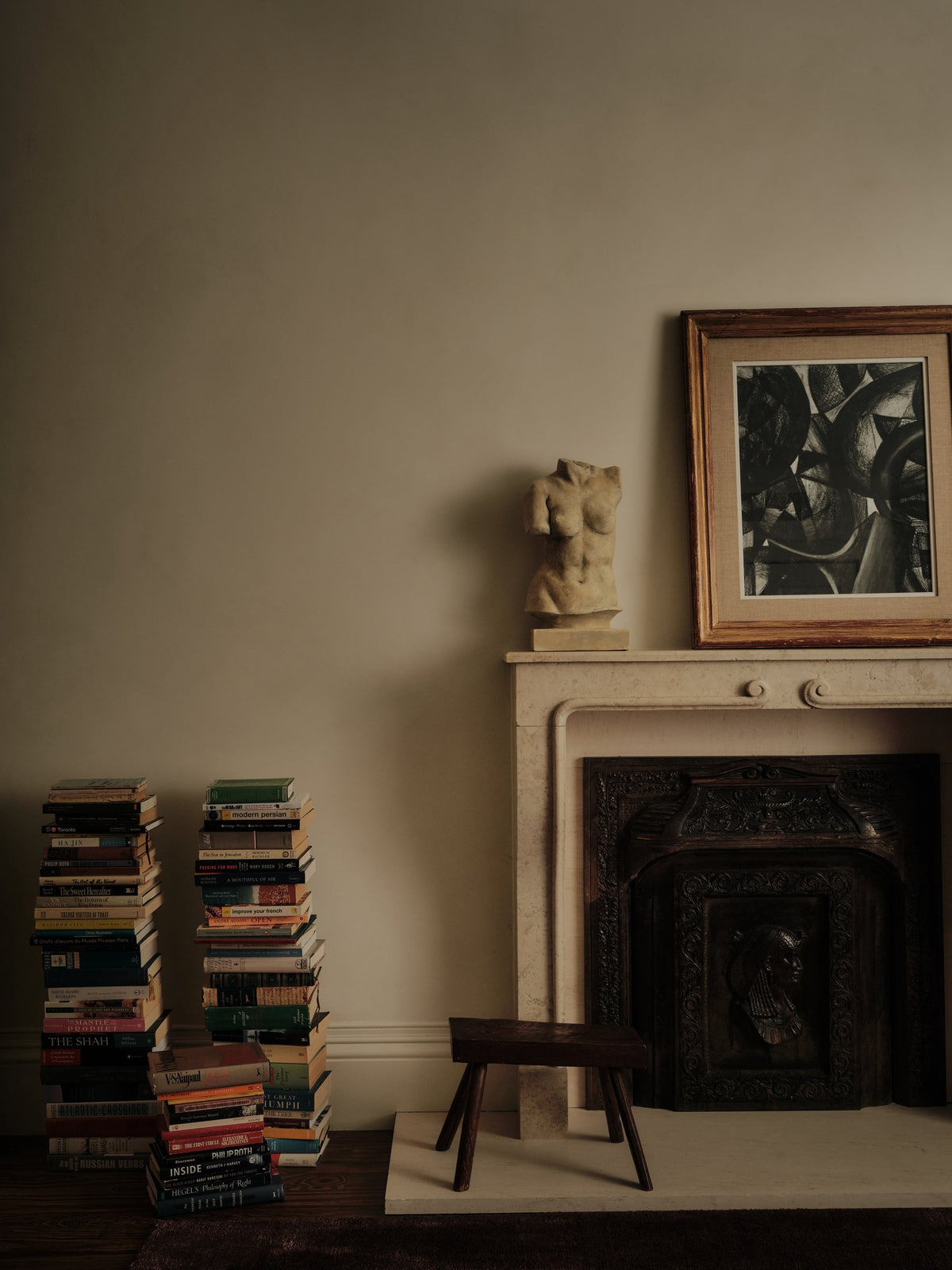 Library corner with stacked vintage books, a carved stone bust and framed artwork above a fireplace