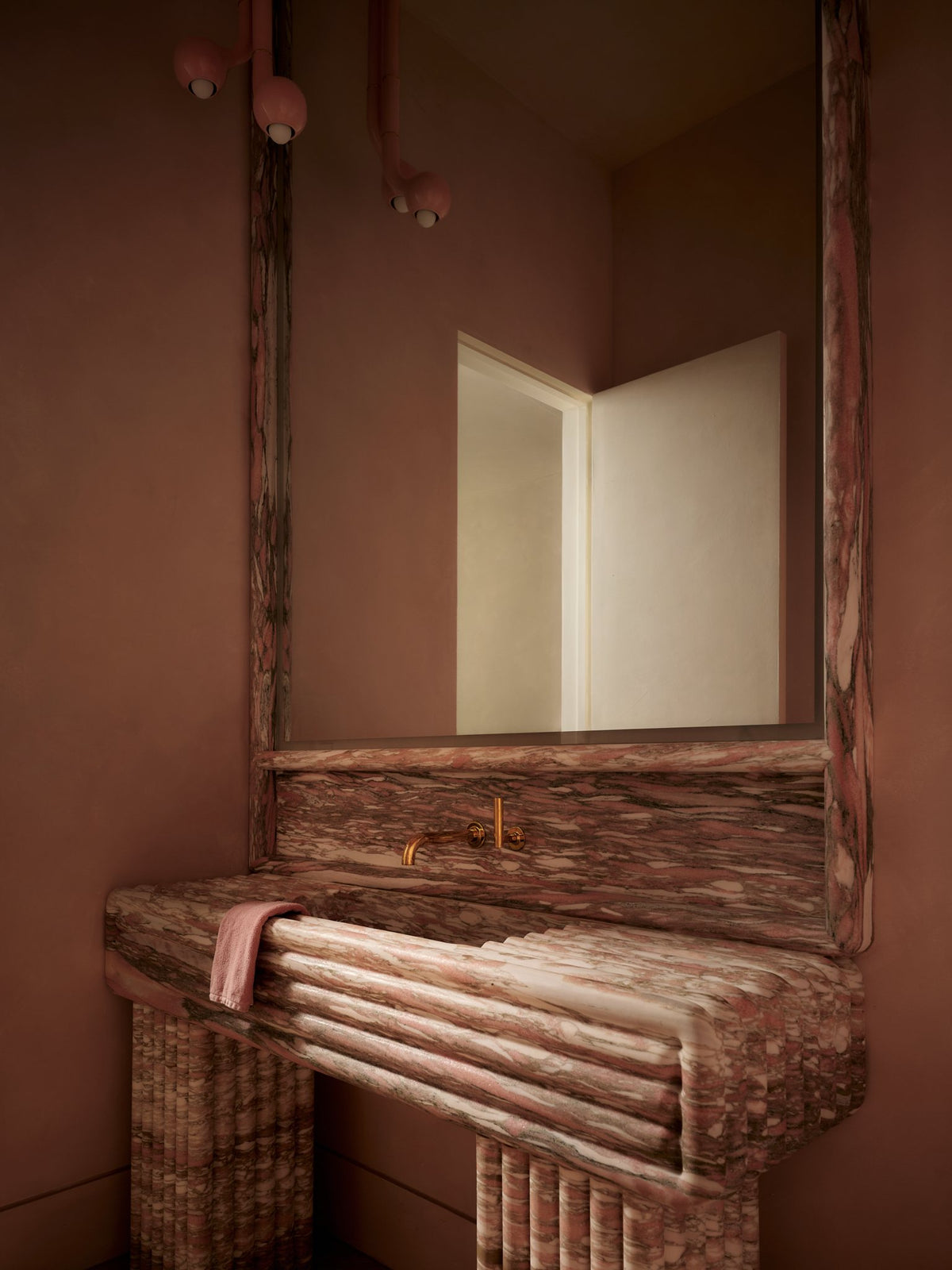Burgundy marble console with a reeded stone base beneath a recessed mirror in a deep red room
