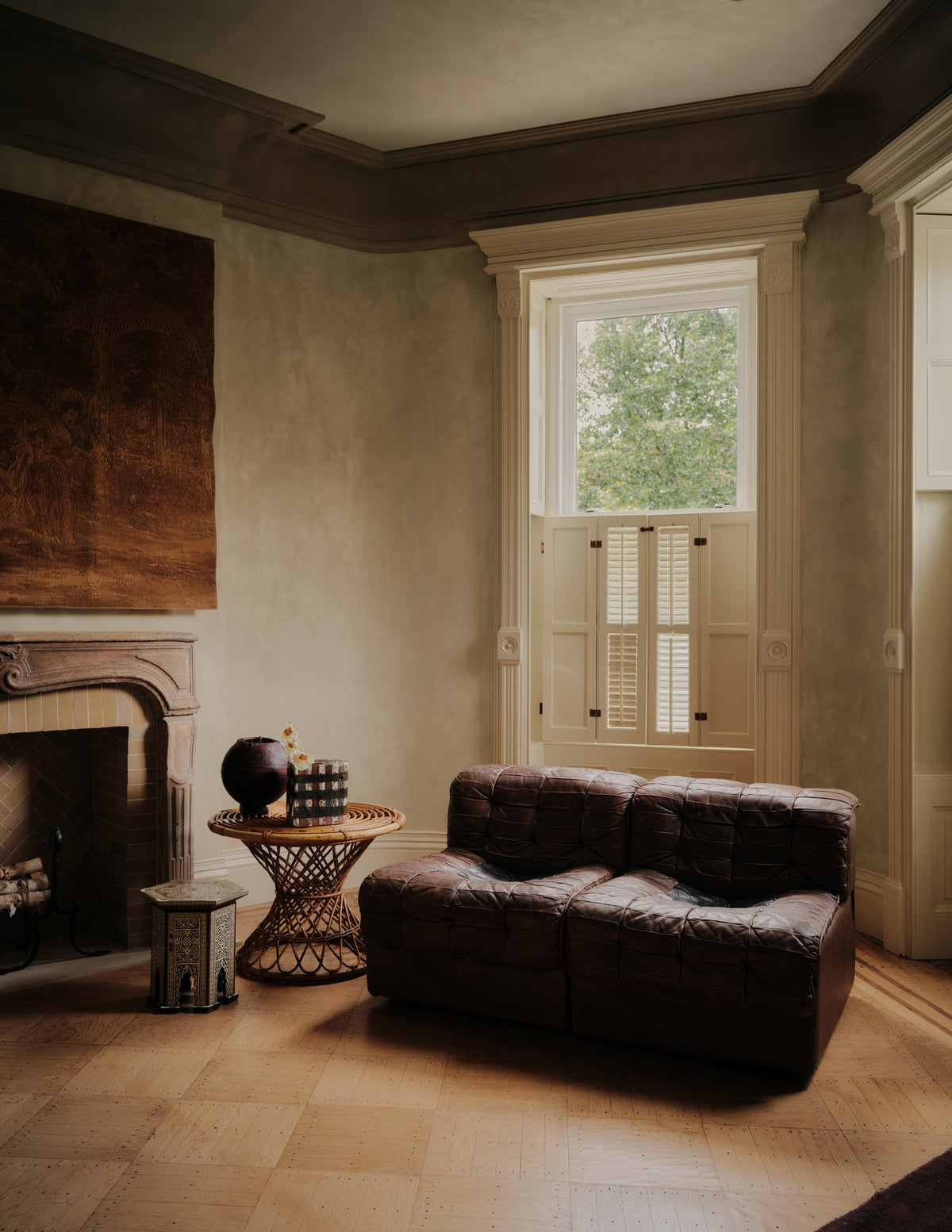 Sitting room with a low leather sofa, rattan side table and tall shuttered window